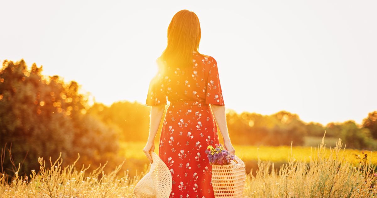 silohuette of woman walking towards sunset in a field